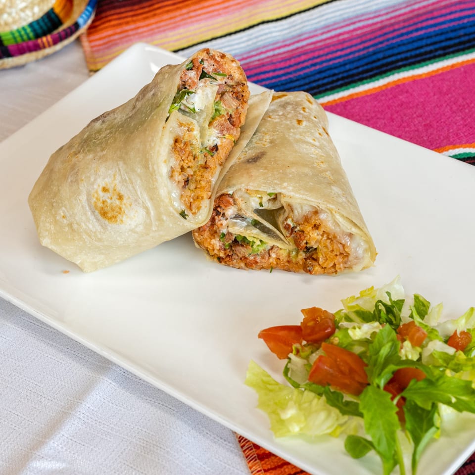 Two large burritos with meat, rice, and sauce, served with a side salad on a white plate.